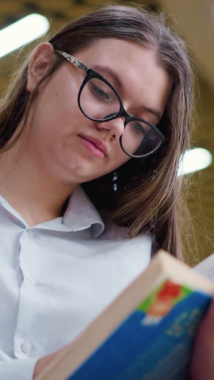 Primer plano de una mujer pensativa con gafas, leyendo un libro con atención, con una bolsa de compra rosa borrosa al fondo, en un animado centro comercial