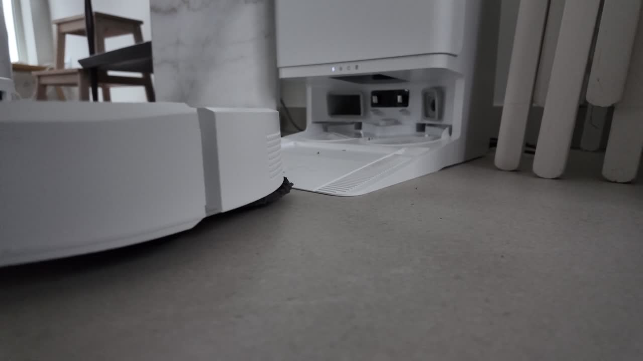 Robotic floor cleaner approaching its docking and cleaning base on a tiled floor