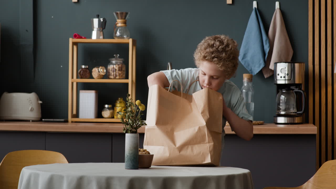 A young boy unpacks a paper delivery bag on a kitchen table