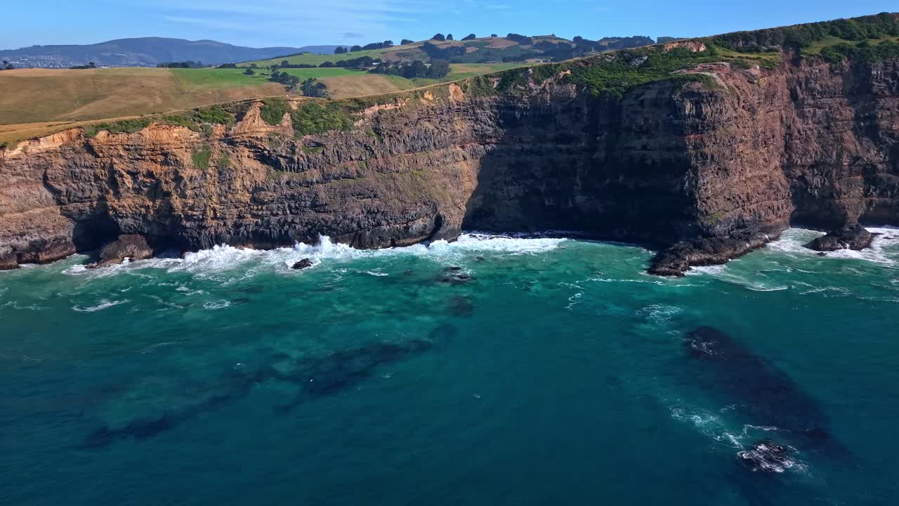 Drone shot pulling back to reveal the coastline and volcanic cliffs of Māori Head, located on the eastern side of Smaills Beach on the Otago Peninsula, Dunedin