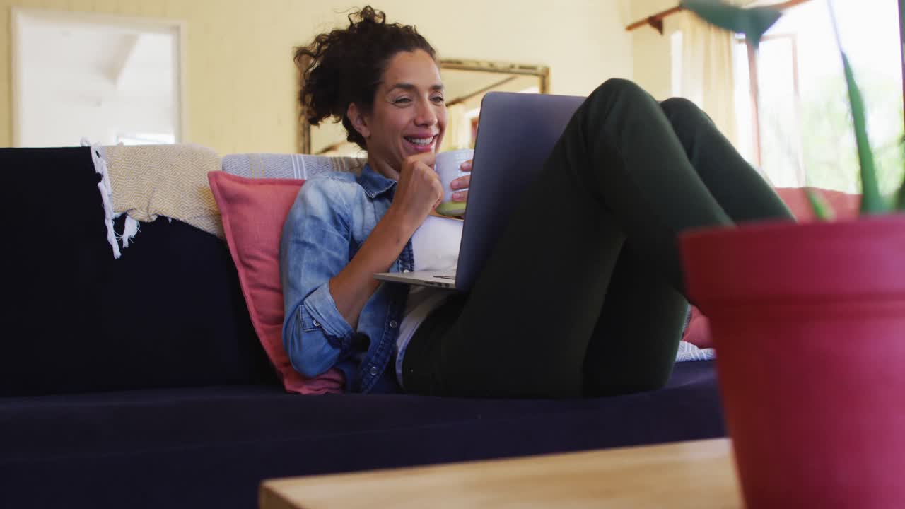 Smiling caucasian woman using laptop on video call, sitting on sofa at home