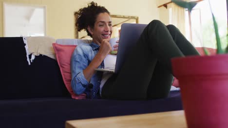 mujer caucásica sonriente usando una computadora portátil en una videollamada, sentada en el sofá en casa