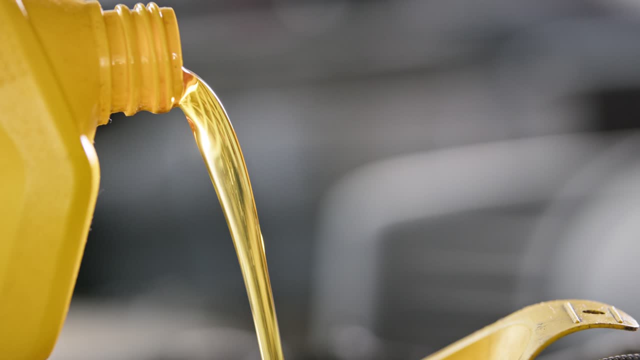 Slow-motion close-up of golden motor oil being poured into an engine.