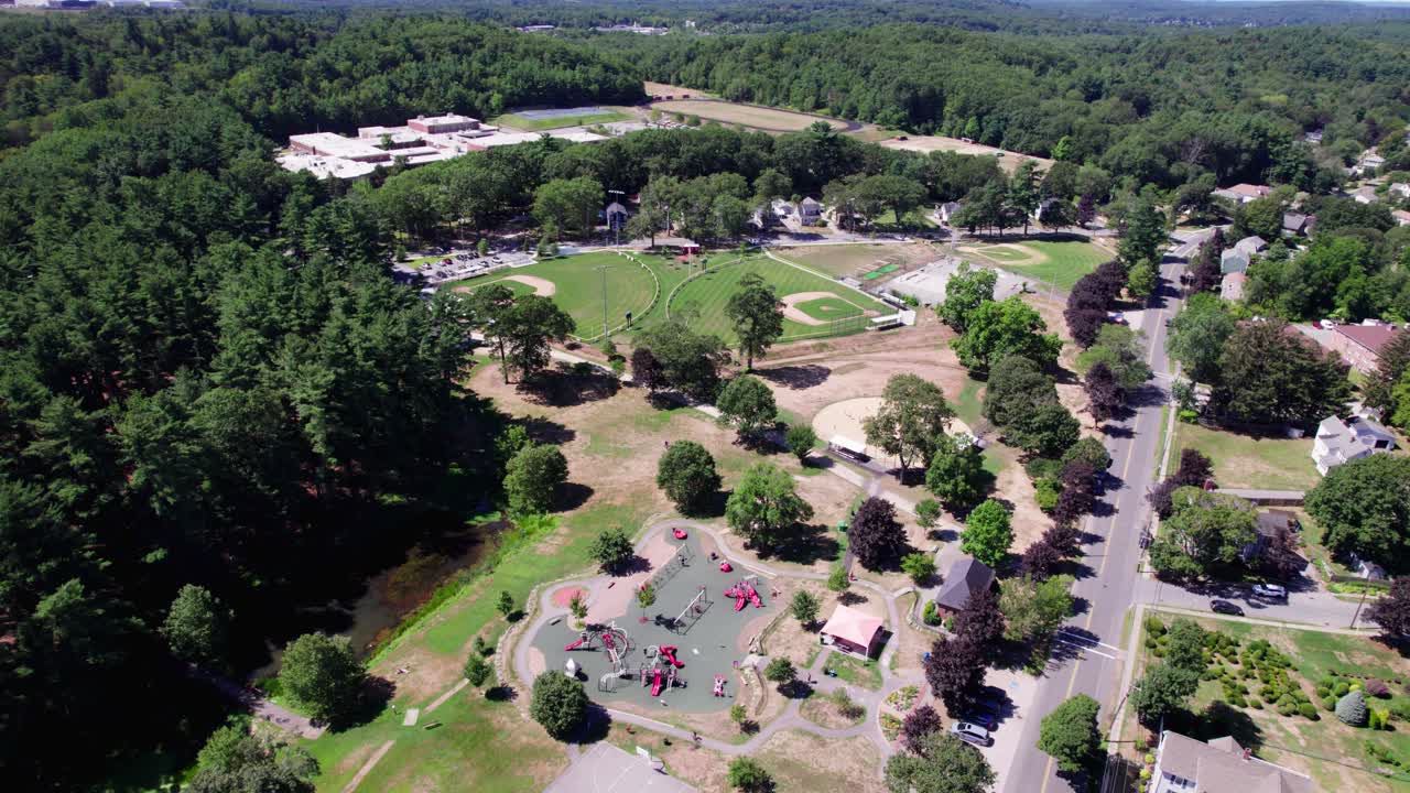 Wide aerial view of a recreational field area in Amesbury, Massachusetts. Three baseball diamonds, a skatepark and a playground are seen, with cars passing by along the border