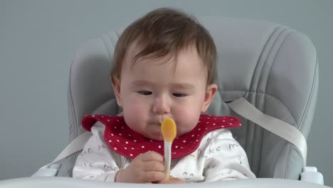 cute baby eating rice porridge meal from a spoon while sitting and a baby chair