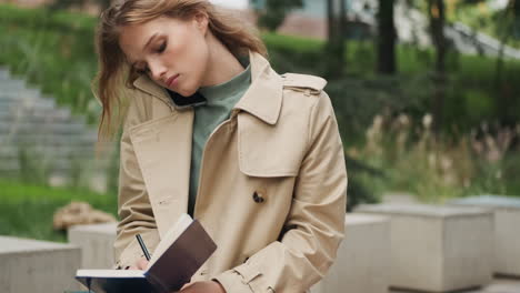 caucasian female student talking on the phone with a notebook in the park.