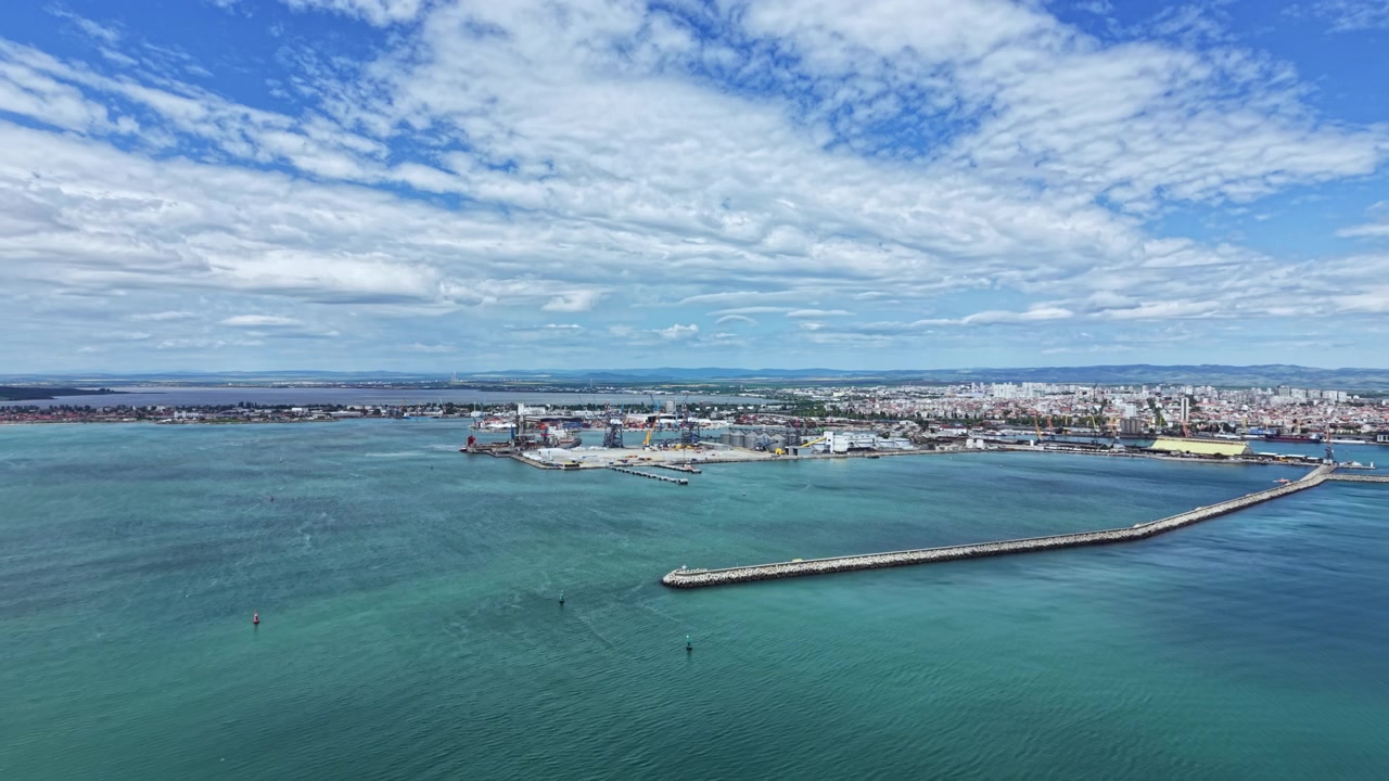 Vista de um porto com céu e água claros, mostrando a área industrial e a costa distante durante o dia