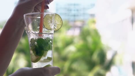 la mano de la mujer agita el cóctel de mojito congelado en un vaso alto