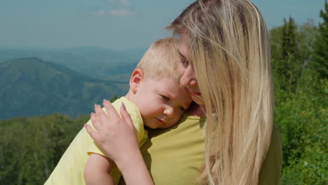 madre cuidadosa calma al hijo soñoliento contra viejas montañas