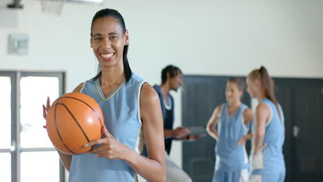holding basketball, woman smiling with teammates in gym, ready for practice