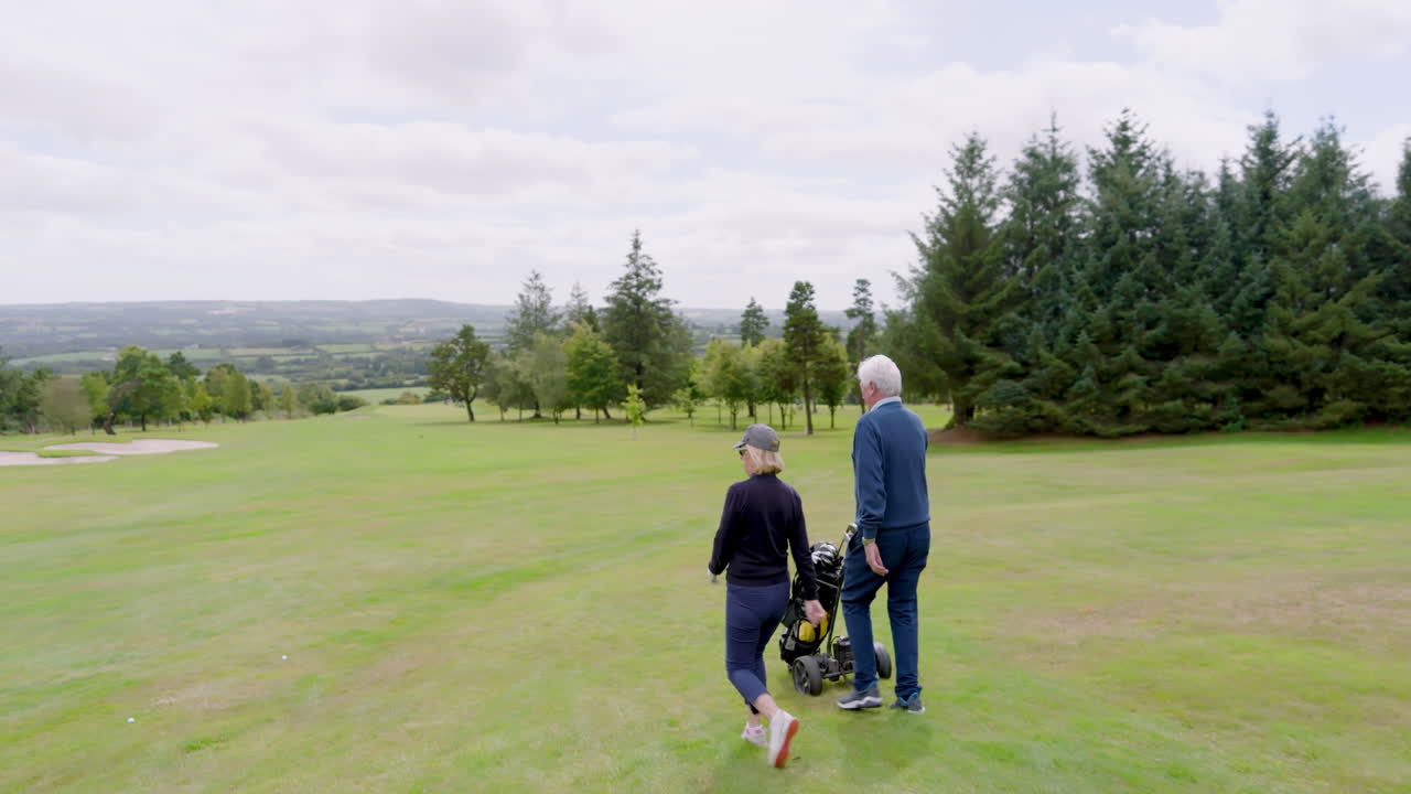 Golf players walking with clubs and talking on golf course on cloudy day, copy space