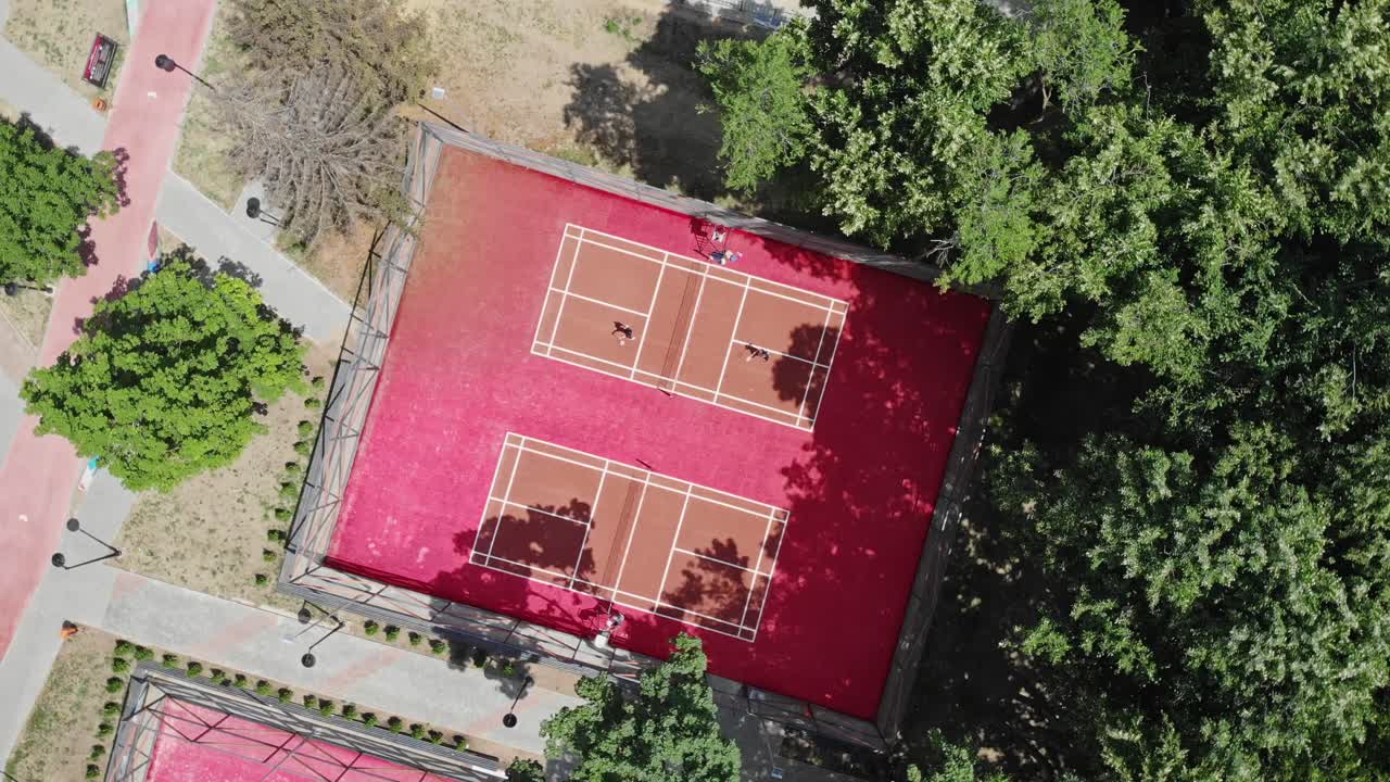 Gente jugando al bádminton en una cancha roja cerca del bosque