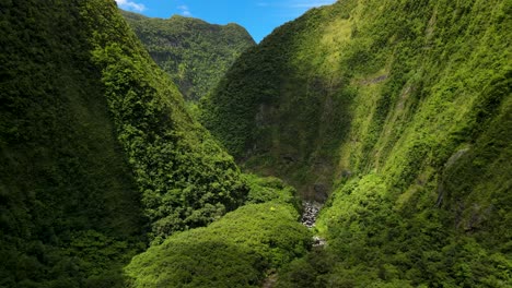 Vista-Aérea-De-Un-Barranco-En-La-Isla-De-La-Reunión,-La-Luz-Del-Sol-Atraviesa-Las-Nubes,-La-Montaña-Está-Cubierta-De-Vegetación-Verde