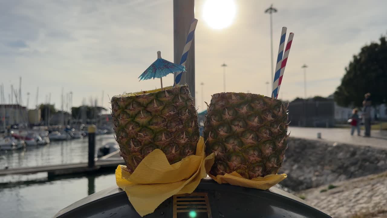 Due bevande tropicali all'ananas con cannucce in una marina soleggiata.