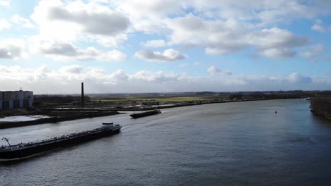 Barcazas-Industriales-Navegando-En-El-Río-Oude-Maas-Bajo-Un-Cielo-Brillante-Con-Suaves-Nubes-Blancas-En-Puttershoek,-Países-Bajos