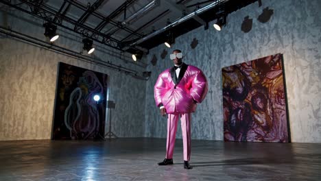 male model showcasing a bold pink inflatable suit and sunglasses, standing confidently in a contemporary art gallery space, illuminated by spotlights and surrounded by large abstract paintings