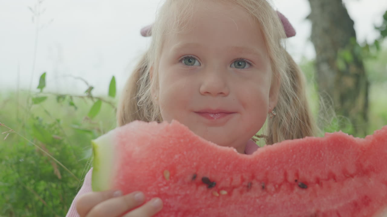 Girl enjoys juicy watermelon, Woman happily eats large juicy watermelon slice outdoors, Joyful female enthusiastically bites into big watermelon in sunny field with playful expression