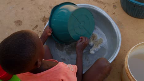 little black cute african child washing dishes in plastic water tank in remote rural village