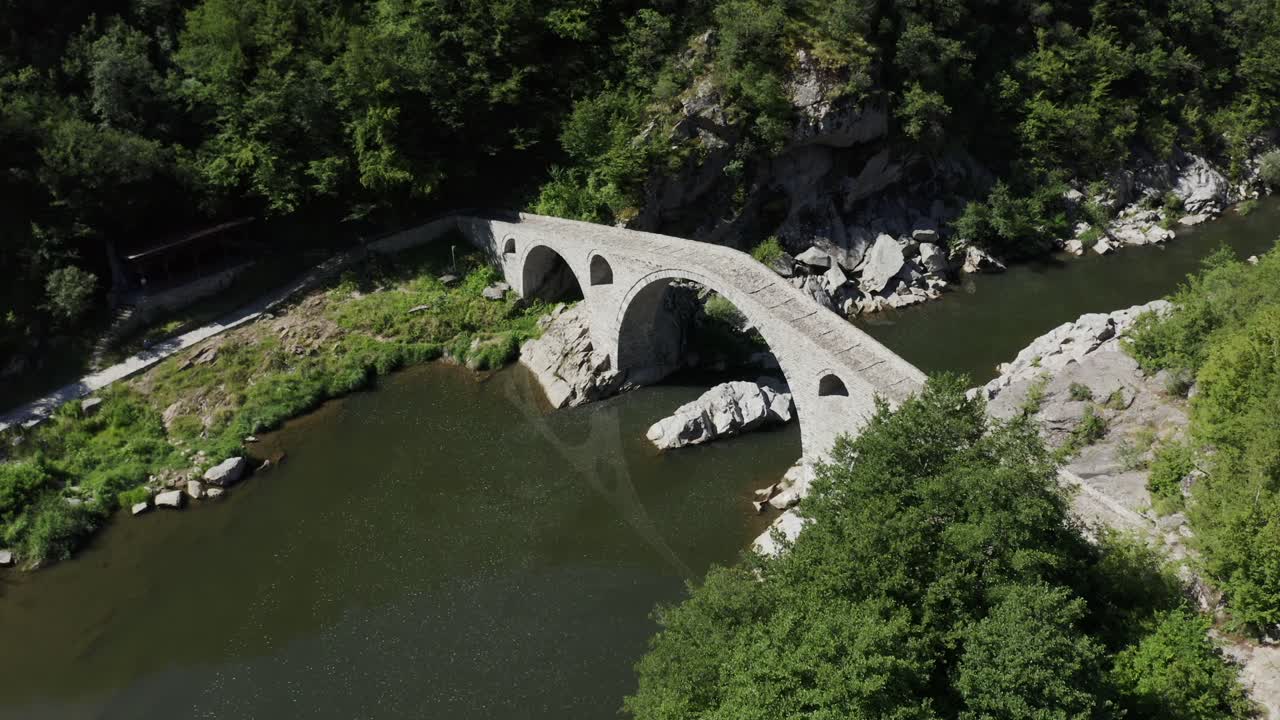 Approaching drone shot moving overhead of the Devil's Bridge and the Arda River, located in the town of Ardino at the foot of Rhodope Mountains in Bulgaria