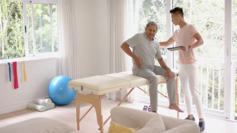 Diverse-male-physiotherapist-with-tablet-examinig-senior-male-patient,-in-slow-motion