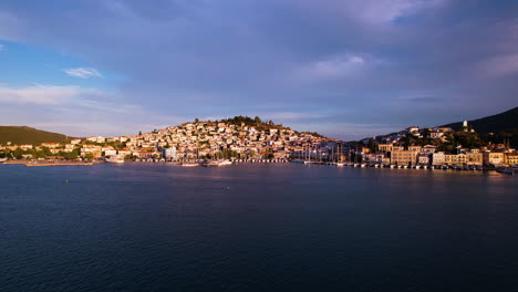 Drohnenflug-über-Das-Griechische-Meer-Mit-Stadtwohnungen-In-Den-Hügeln-Im-Hintergrund