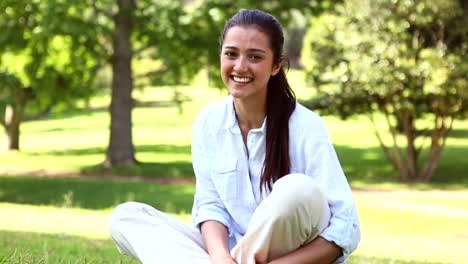 Linda-Chica-Sentada-En-El-Parque-Sonriendo-A-La-Cámara