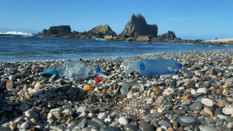 discarded plastic bottles in the ocean surf hitting a pebble beach