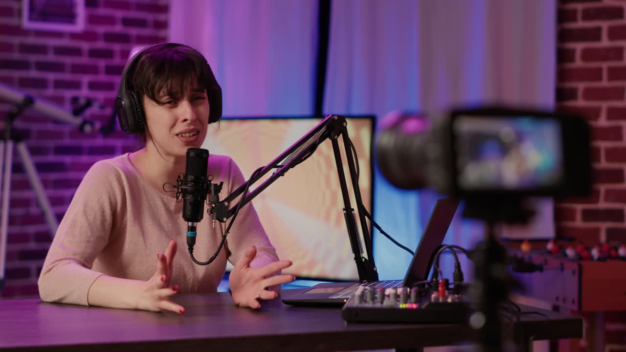 Selective focus on online radio host talking in front of digital camera recording vlog sitting at desk