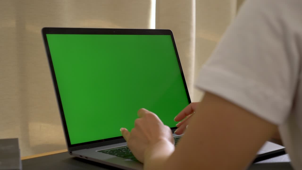 sobre el hombro de la mujer asiática mirando la pantalla verde. persona de la oficina usando una computadora portátil escribiendo en un teclado con una pantalla verde portátil, 4k dolly shot