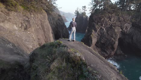Woman-overlooking-Breathtaking-Oregon-Coast-Landscape,-Cinematic-Aerial-Tilt-up-Reveal
