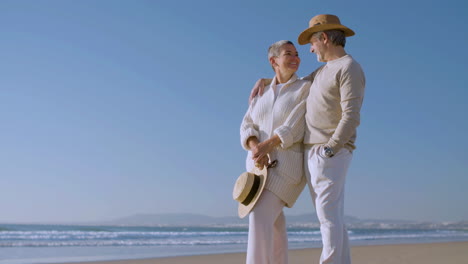 romantic senior man hugging his wife and talking with her on the beach