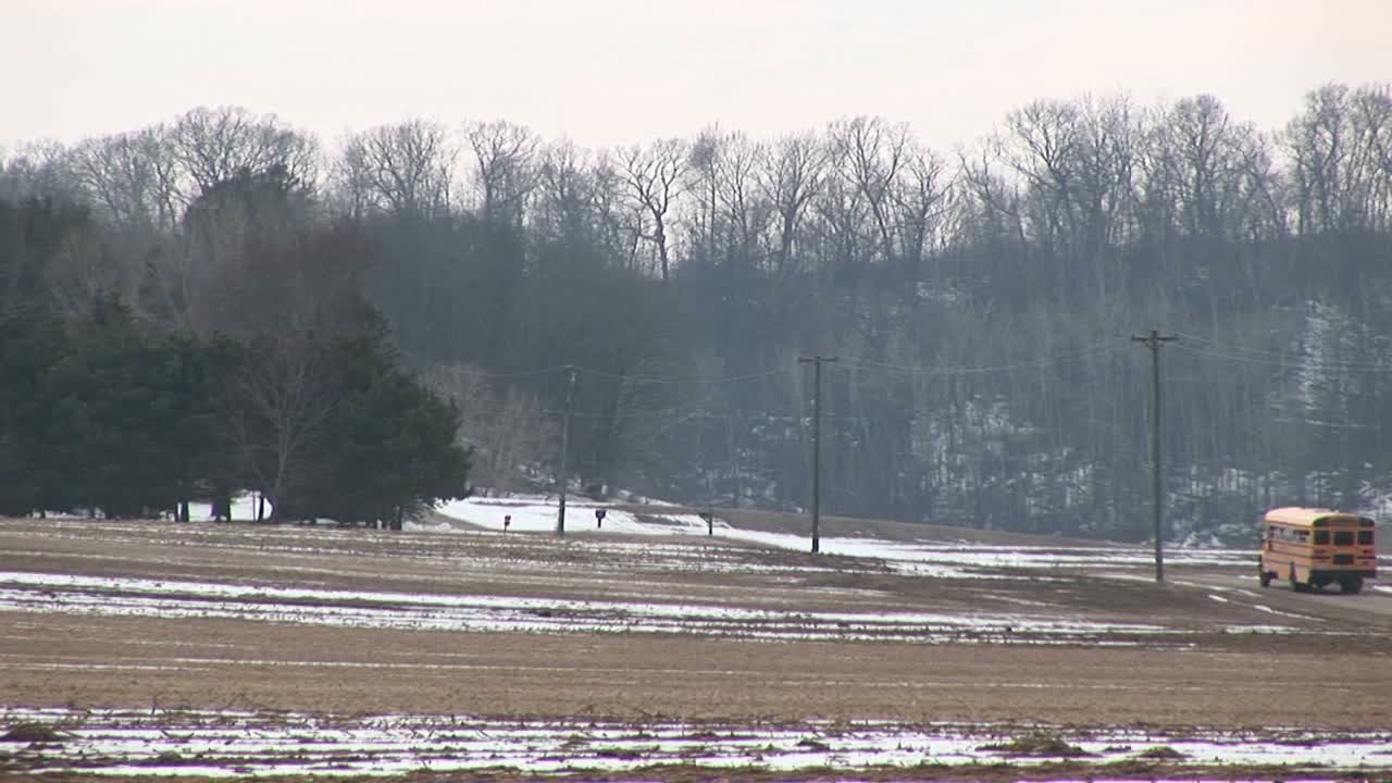 시골길을 따라 아이들을 데리러 가는 밝은 노란색 스쿨버스 정류장