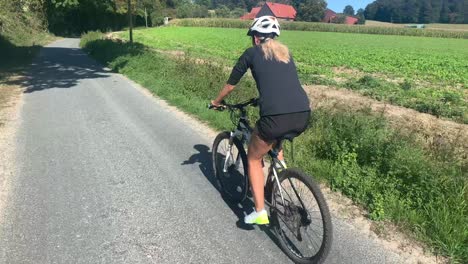 Blond-young-girl-with-helmet-is-riding-the-mtb-mountain-bike-on-the-road