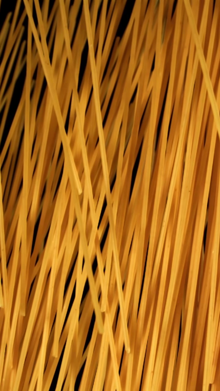 黒い背景に舞い上がる黄金色のスパゲッティパスタ