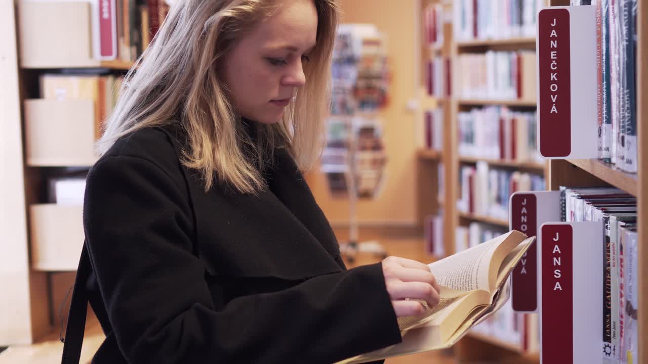 Caucasian female is picking up one book from library and reading few pages