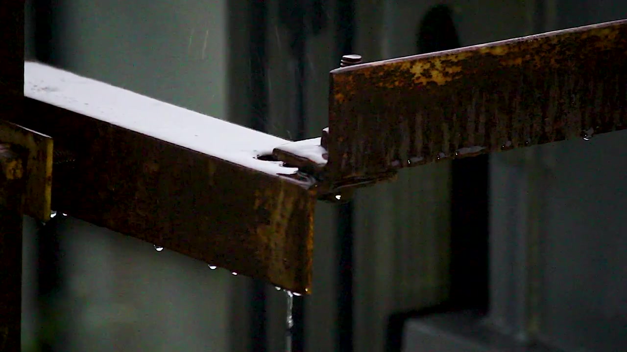 Rusty industrial metal structure collects rainwater and releases dripping streams during rainfall, useful for weather, corrosion, infrastructure, maintenance and environmental projects.
