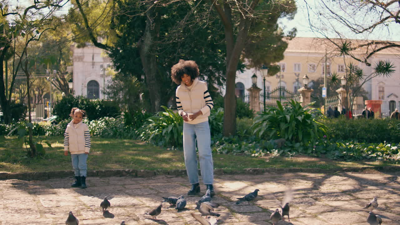 사랑스러운 딸과 함께 아름다운 녹색 공원에서 서있는 음식 비둘기를 던지는 여자.