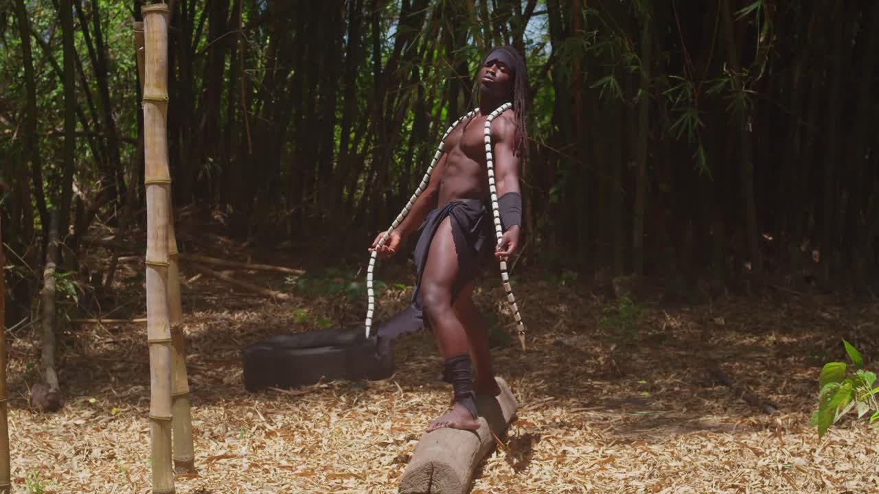 A muscular man with dark skin, dressed in a Tarzan cosplay costume, stands amidst a lush forest.