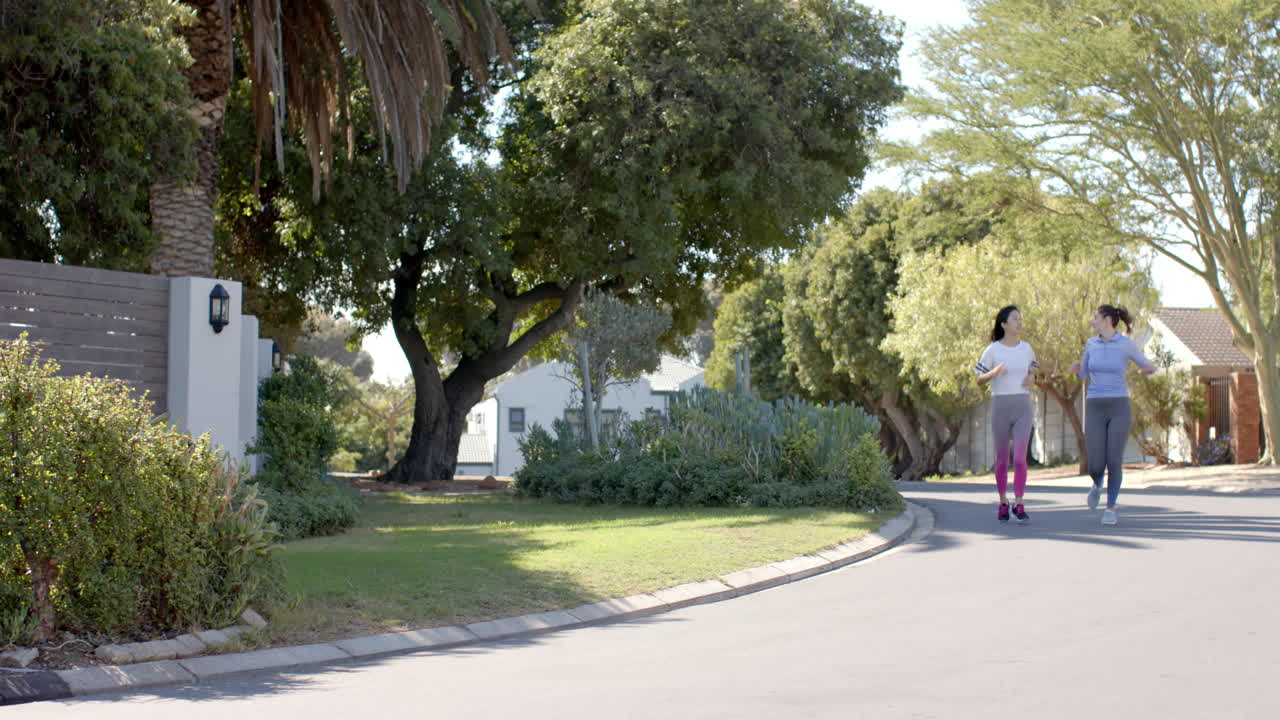 Jogging together, two women friends exercising in suburban neighborhood outdoors