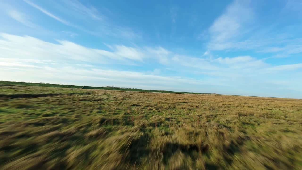 Volo ad alta velocità di un drone FPV sopra zone umide e argini allagati nella Lincolnshire rurale, catturando il rigoglioso paesaggio primaverile dall'alto.
