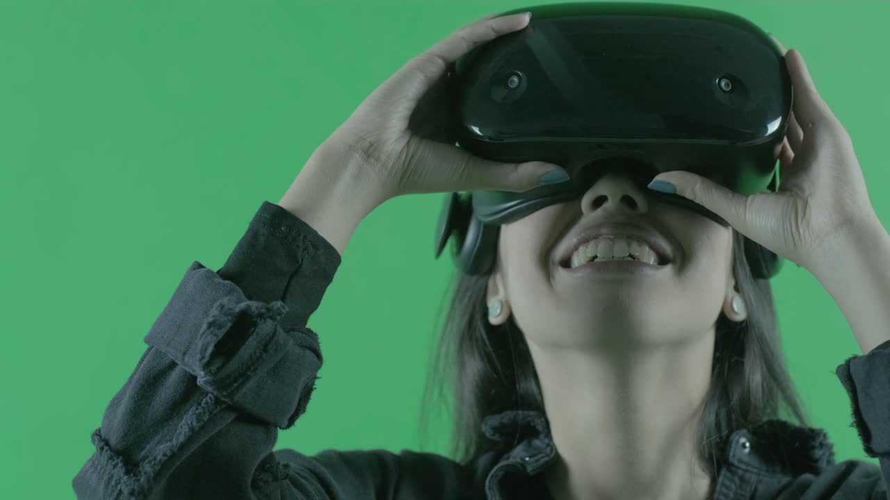 joven hermosa se pone, mira a su alrededor y se pregunta cómo increíble en el auricular vr. casco de realidad virtual en el fondo verde. llave de croma