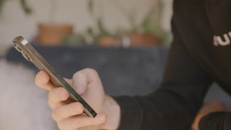 side angle of a man scrolling and swiping and typing on an iphone with a couch in the background