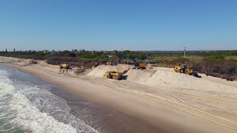 Aerial-shot-of-the-ocean-water-with-excavators-in-the-back-clearing-the-sand