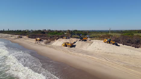 Toma-Aérea-Del-Agua-Del-Océano-Con-Excavadoras-En-La-Parte-Trasera-Limpiando-La-Arena