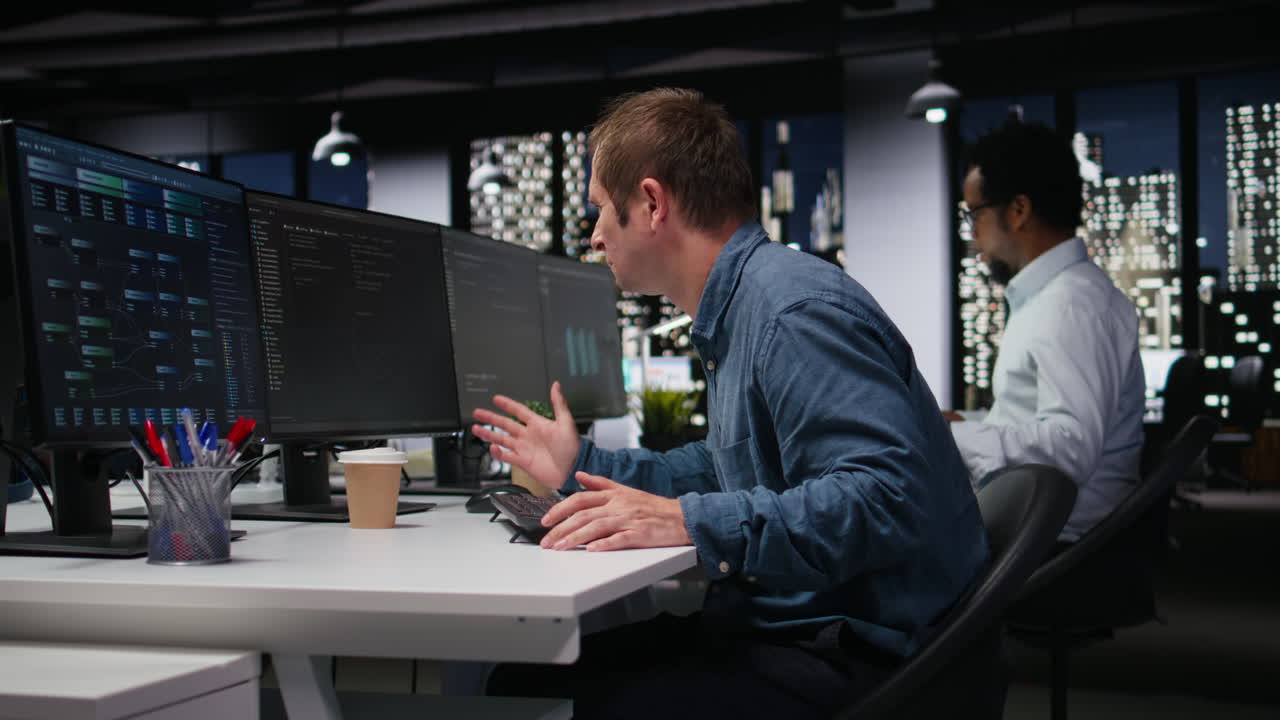 Male Programmer Working on Multiple Computer Screens in Modern Office at Night