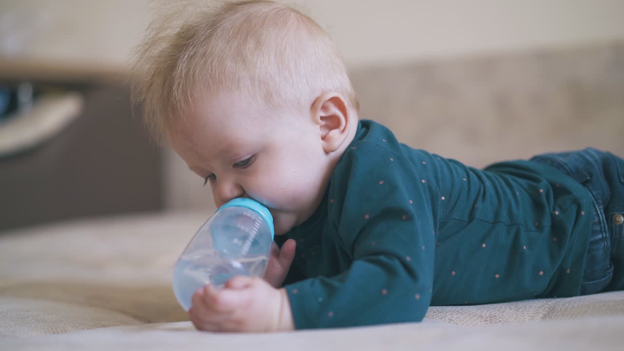 adorable niño mordisquea la tetita de la botella acostado en la cama suave en la habitación