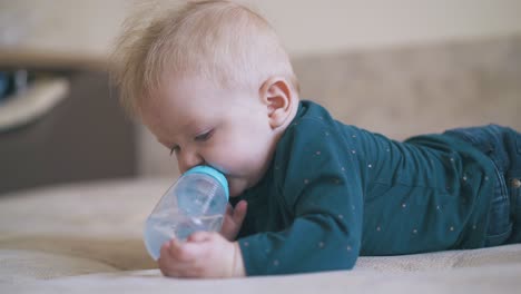 adorable boy nibbles bottle teat lying on soft bed in room