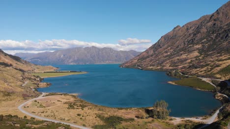 Aerial-drone-shot-of-a-blue-majestic-lake-surrounded-by-mountains-in-New-Zealand-on-sunny-summer-day-in-4k