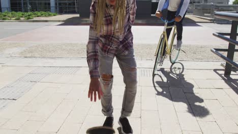 two diverse male friends riding a skateboard and bicycle in the street