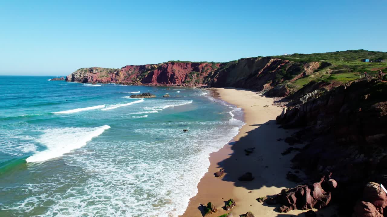 Onde del mare che si infrangono sulla riva sabbiosa di una spiaggia vicino alle scogliere rocciose. - Ripresa aerea.